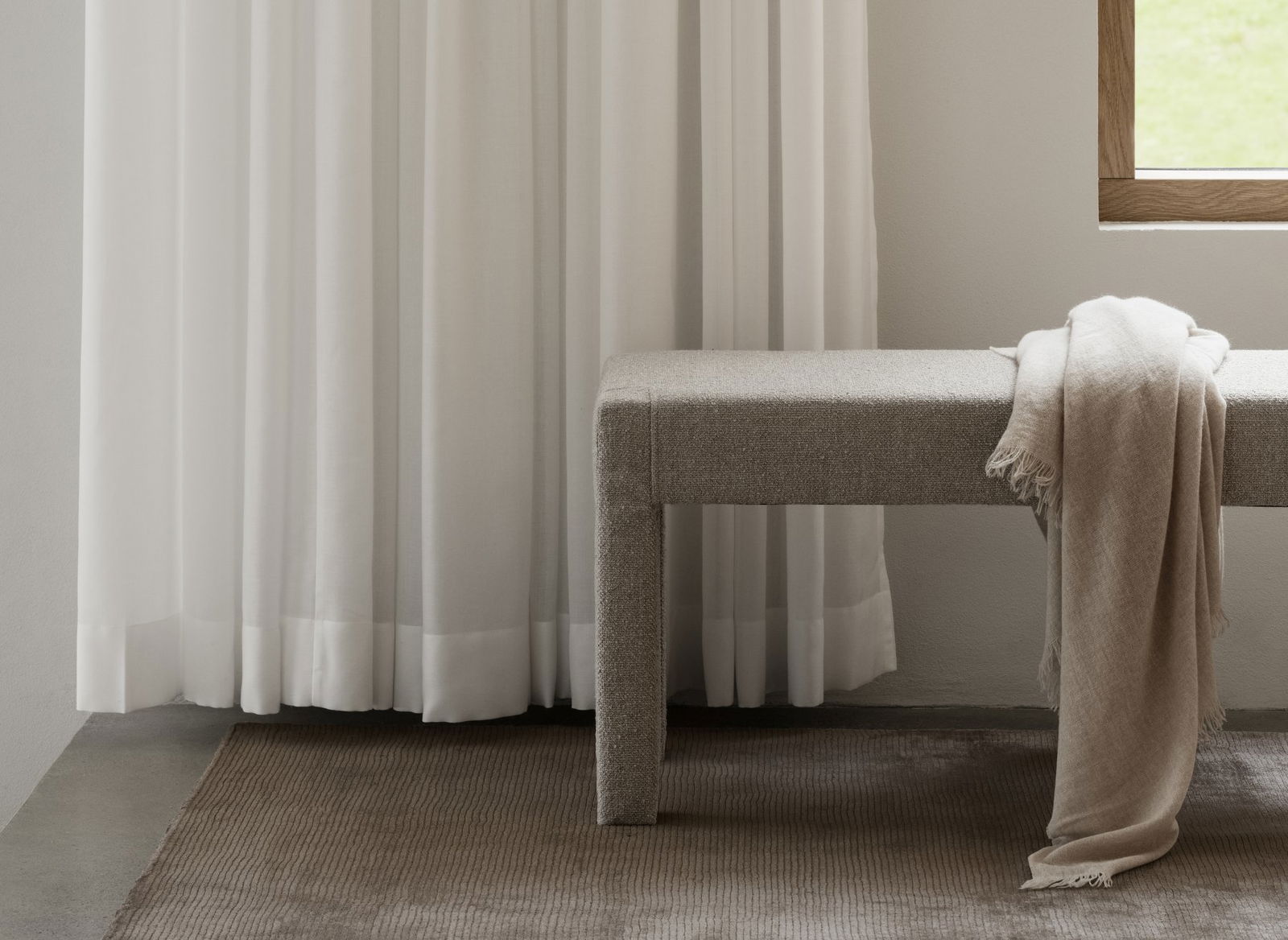 Cozy interior featuring a textured bench beside flowing white curtains and a soft blanket.