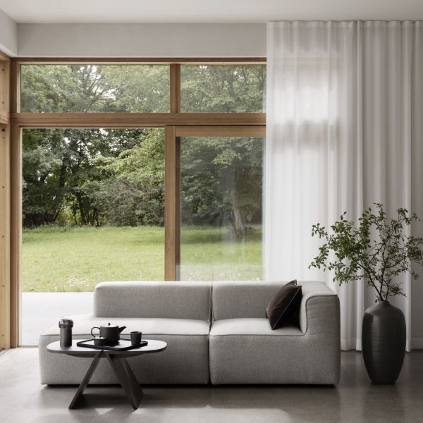 Stylisches modernes Wohnzimmer mit grauem Sofa, Kaffeetisch und großen Fenstern mit Blick auf das Grüne.