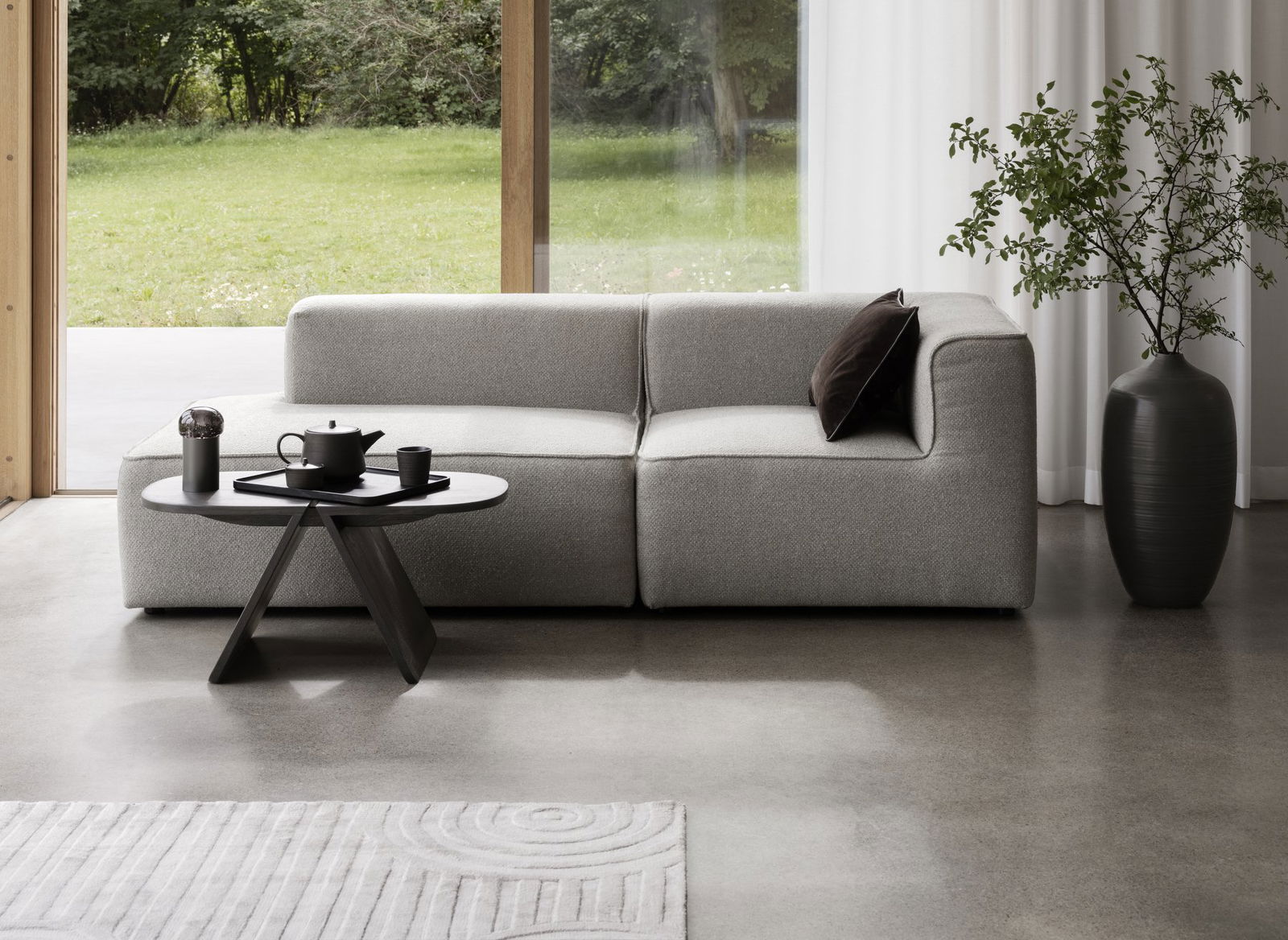 Modernes Wohnzimmer mit einem grauen Sofa, einem Couchtisch und Pflanzen außen.