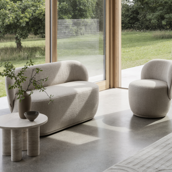 Moderner Wohnraum mit minimalistischem Sofa und Stuhl, akzentuiert durch natürliches Licht und Pflanzen.
