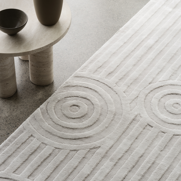 Strukturierter neutraler Teppich mit kreisförmigen Mustern neben einem minimalistischen Tisch und einer Schüssel.