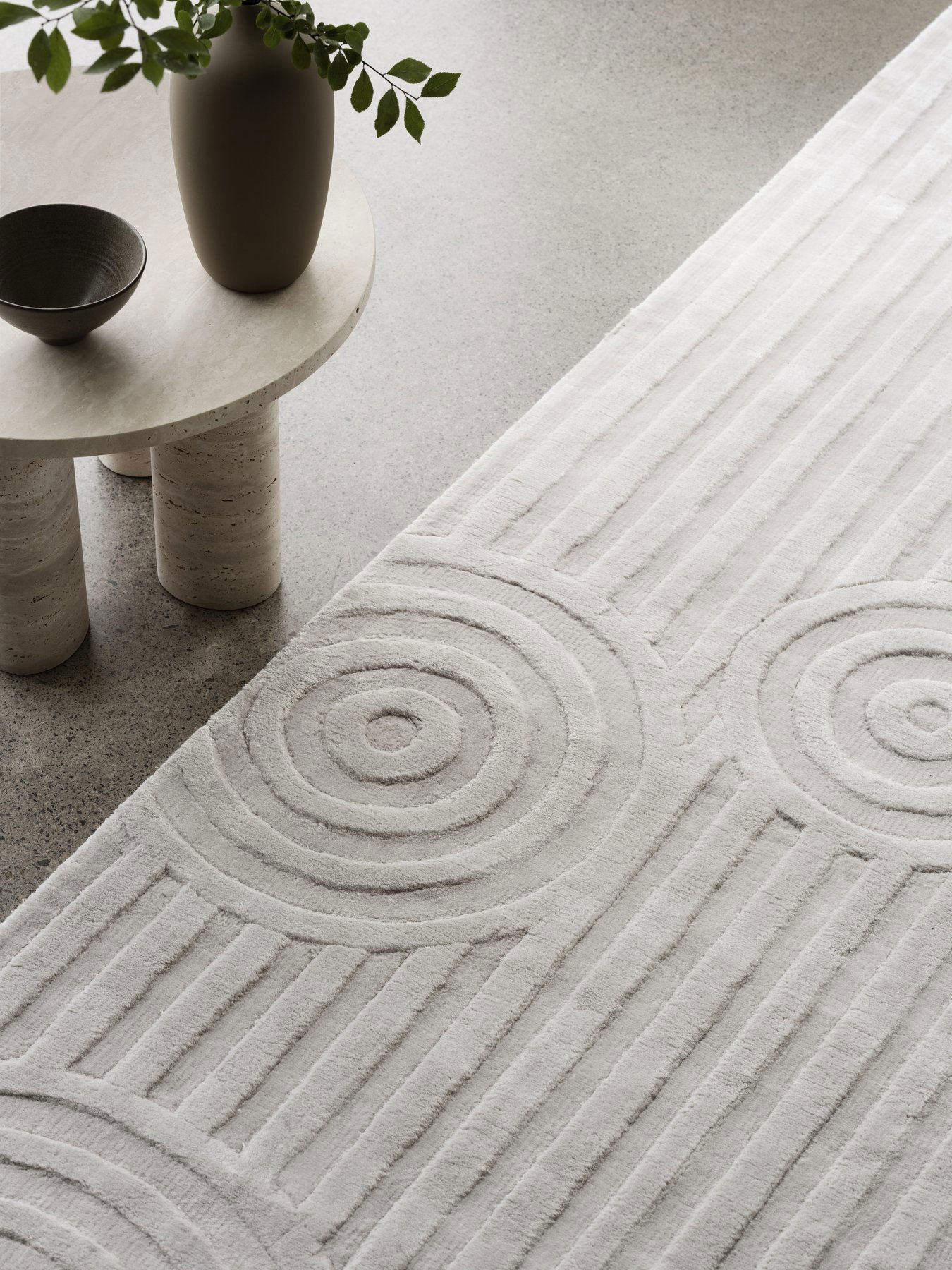Strukturierter neutraler Teppich mit kreisförmigen Mustern neben einem minimalistischen Tisch und einer Schüssel.