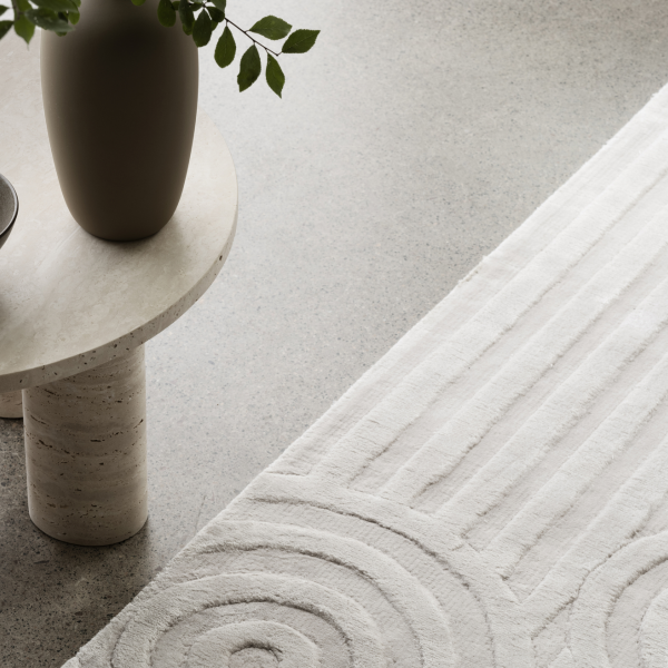 Minimalistische Wohnzimmerdekoration mit einer Vase und einem strukturierten Teppich auf einer hellen Fläche.