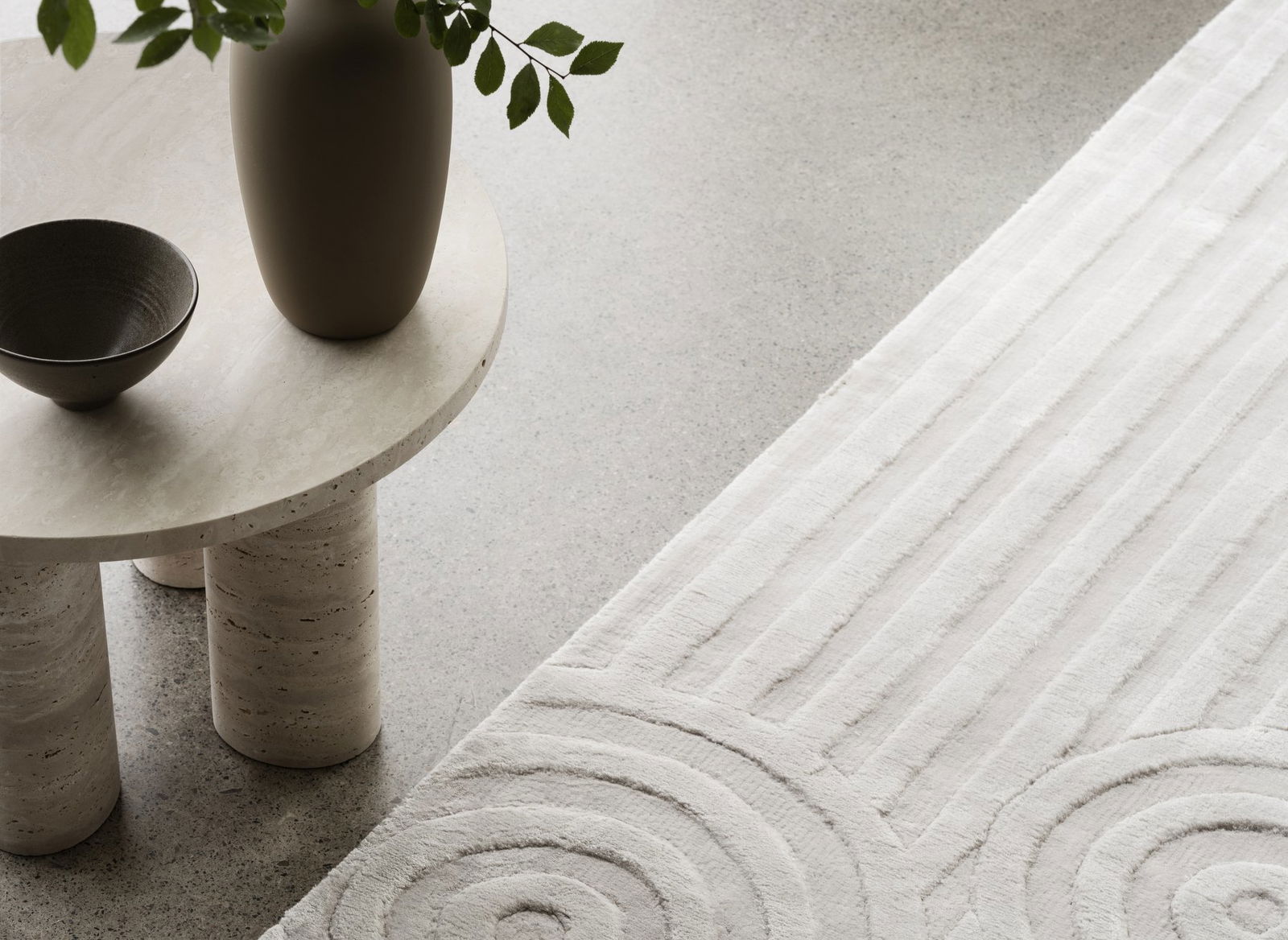 Minimalistische Wohnzimmerdekoration mit einer Vase und einem strukturierten Teppich auf einer hellen Fläche.