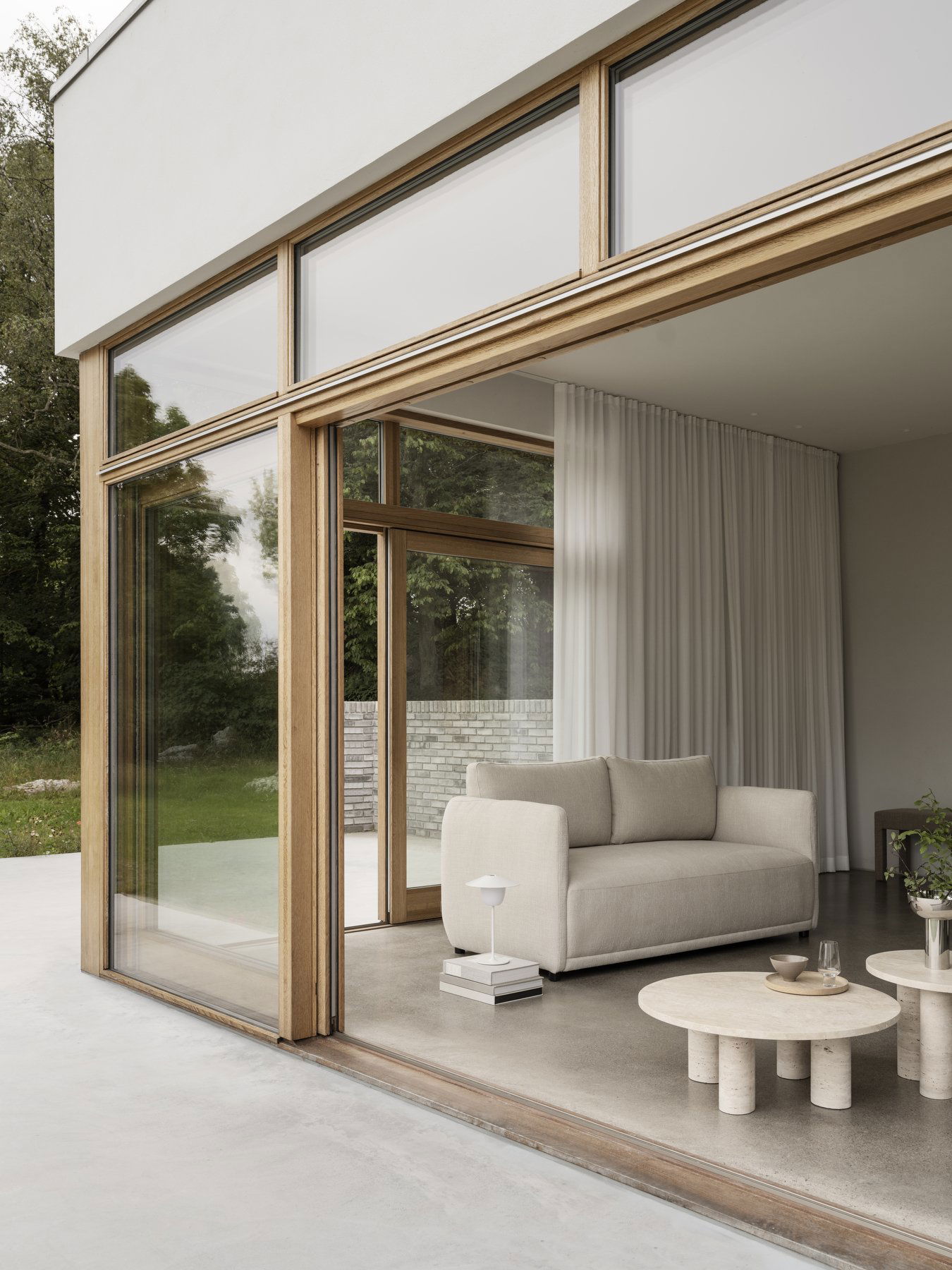 Modernes Wohnzimmer mit einer großen Glaswand, neutralem Sofa und minimalistischer Dekoration.