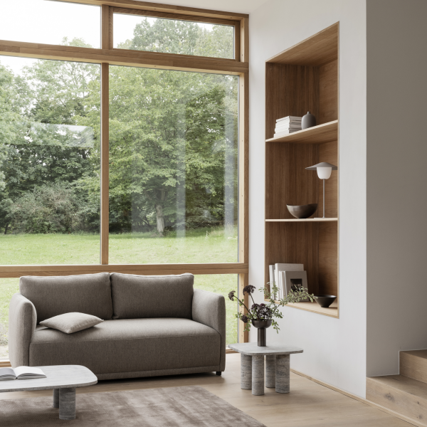 Modern living room with a gray sofa and wooden shelves overlooking a green landscape.