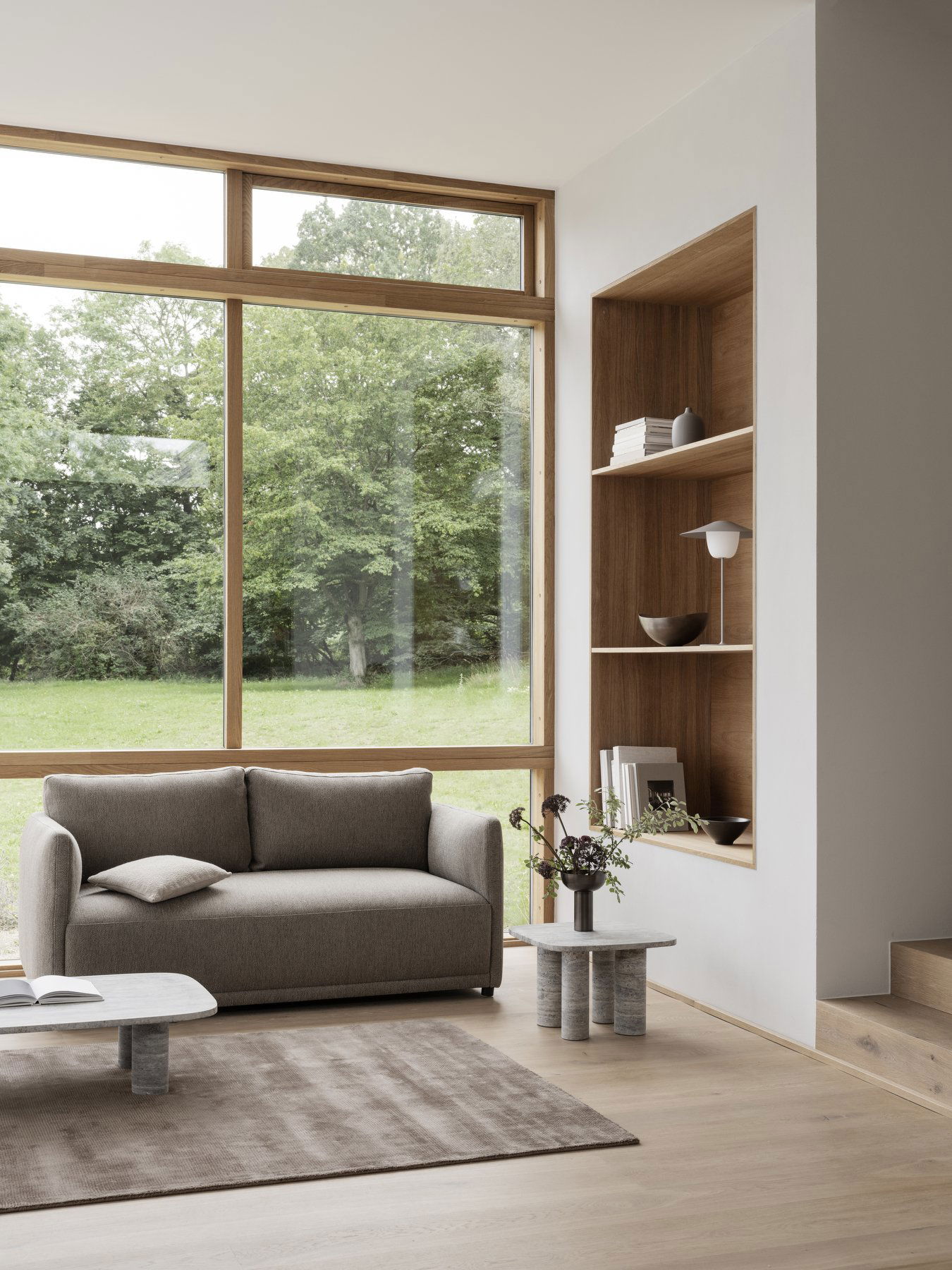Modern living room with a gray sofa and wooden shelves overlooking a green landscape.