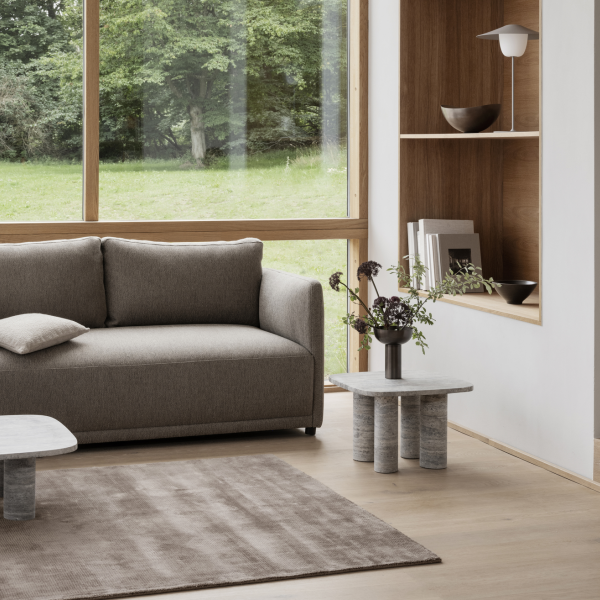 Modern living room with a gray sofa, minimalist decor, and large windows overlooking greenery.