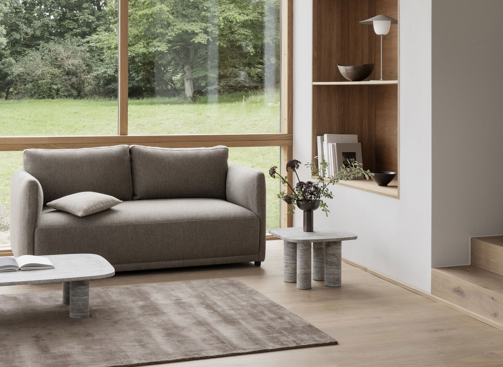 Modern living room with a gray sofa, minimalist decor, and large windows overlooking greenery.