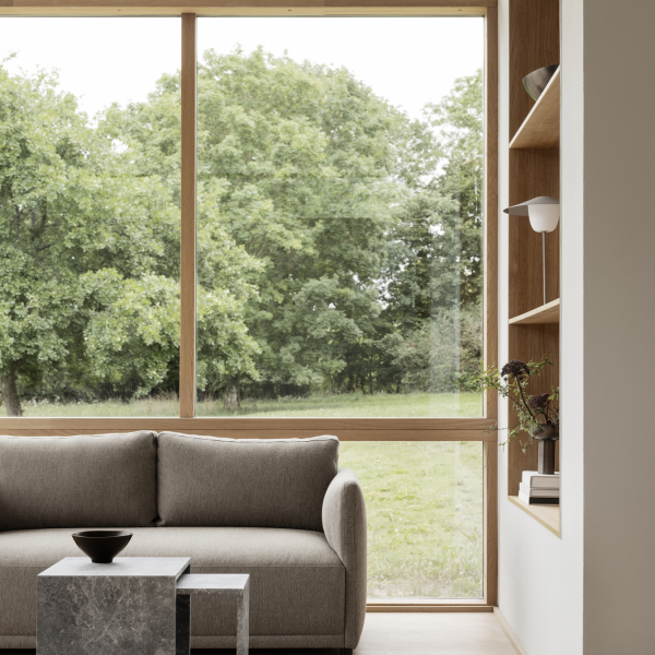 Modern living room with a gray sofa, stylish decor, and large windows overlooking greenery.
