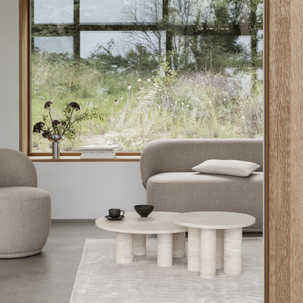Moderner Wohnraum mit einem minimalistischen Sofa, einem runden Couchtisch und grünen Pflanzen draußen am Fenster.