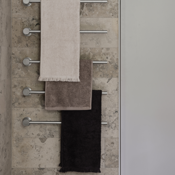 Weiche, luxuriöse Handtücher hängen an einem eleganten Metallregal vor einer strukturierten Steinwand.