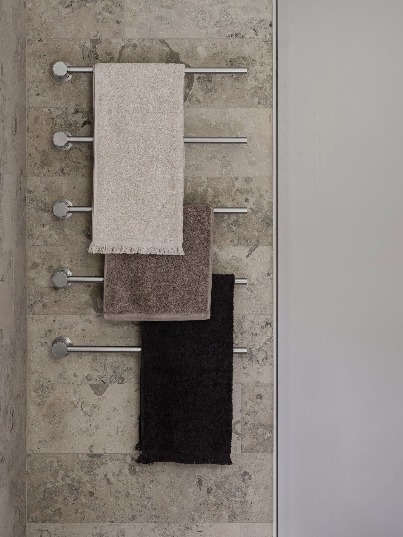 Weiche, luxuriöse Handtücher hängen an einem eleganten Metallregal vor einer strukturierten Steinwand.