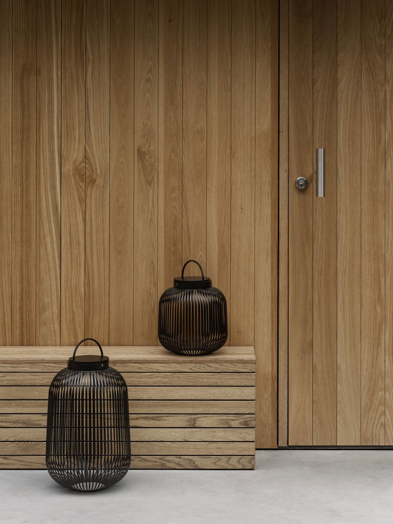 Stylische Außenlaternen auf einer Holzbank neben einer modernen Holztür.