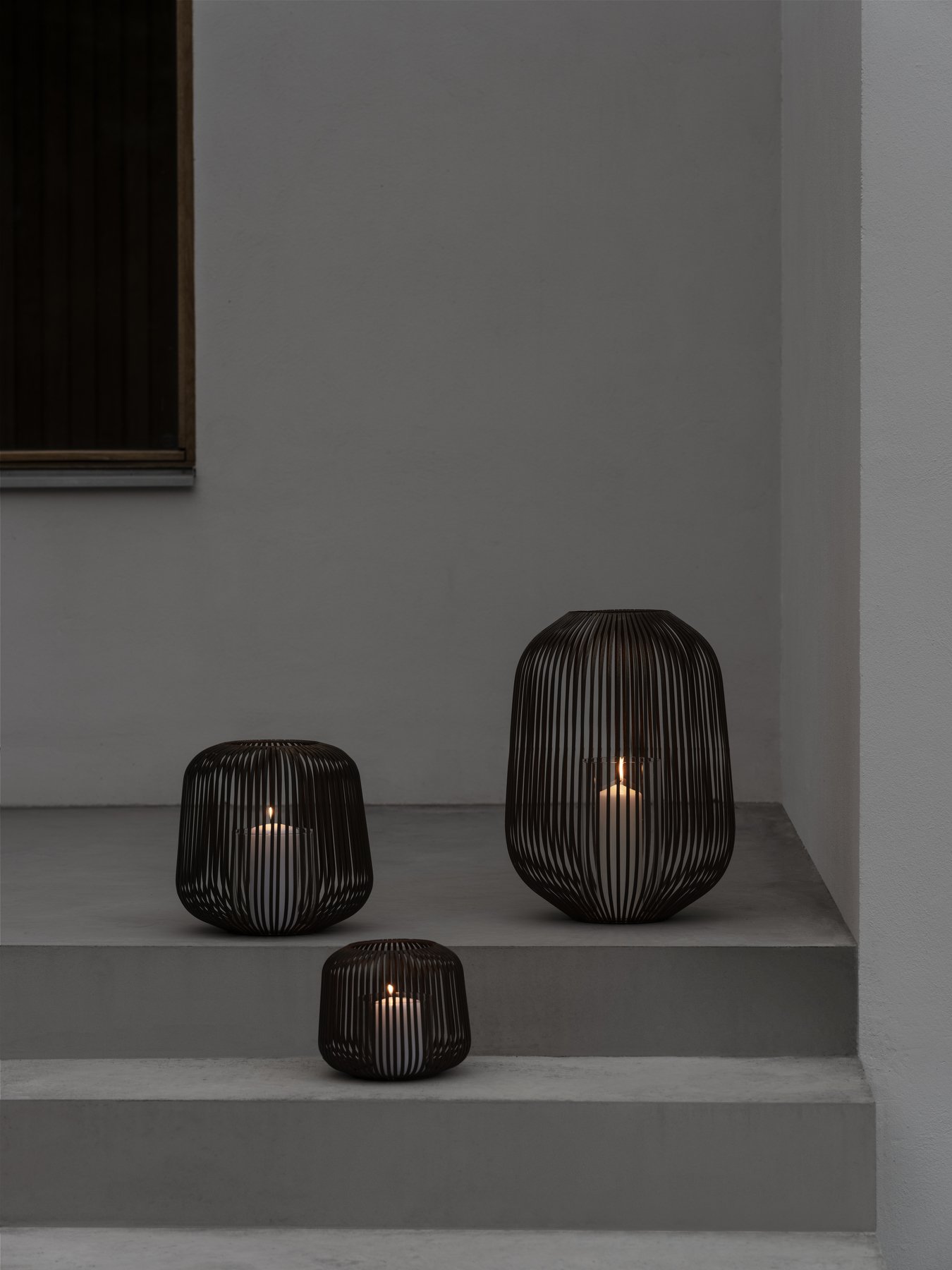 Elegante schwarze Drahtgeflecht-Laternen mit Kerzen auf minimalistischen Außentreppen.
