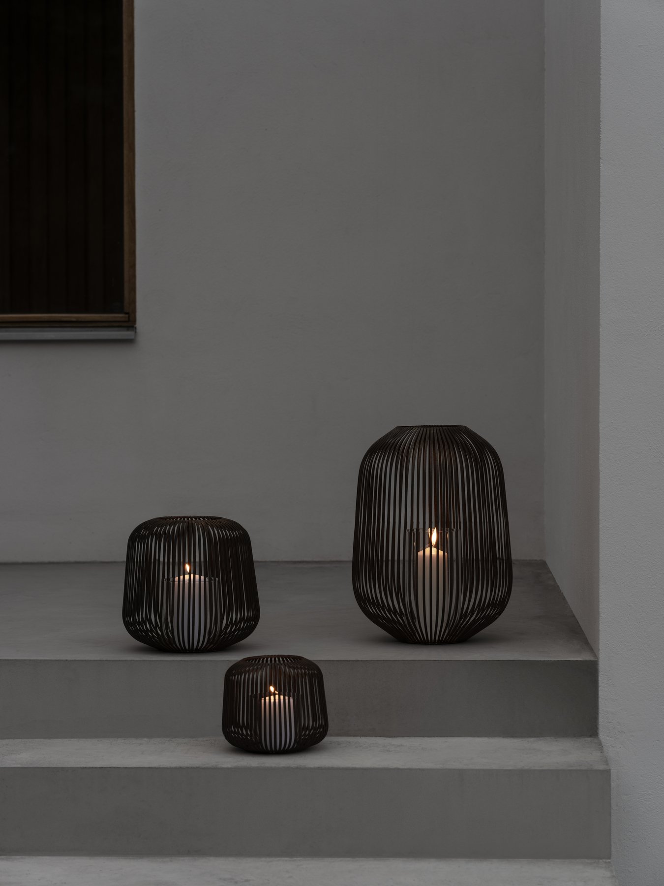 Stilvolle schwarze Drahtlaternen mit Kerzen auf modernen Betontreppen.