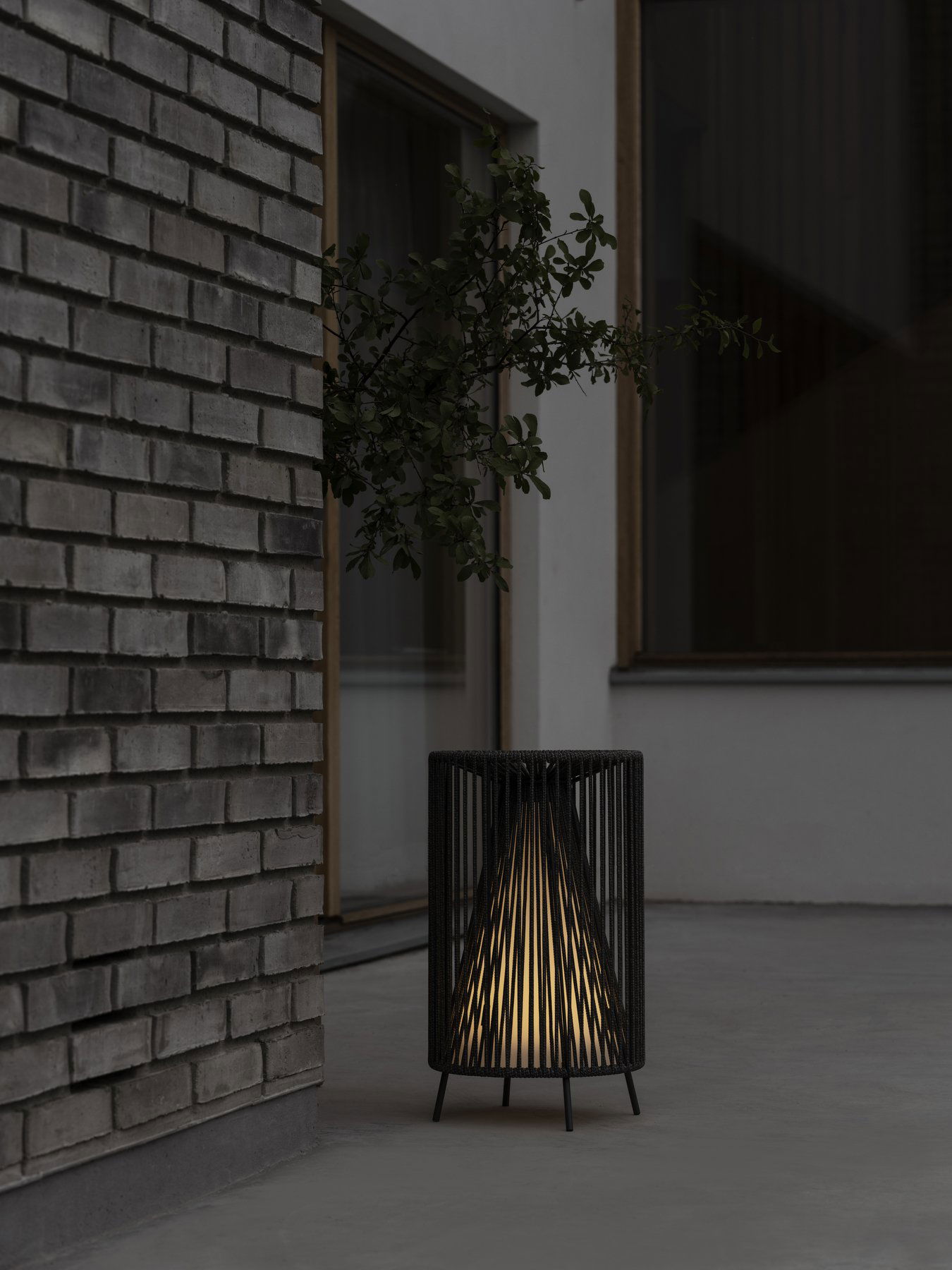 Moderne schwarze Lampe mit leuchtendem Innenraum, platziert neben einer strukturierten Backsteinmauer.