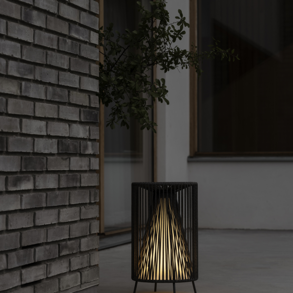Moderne schwarze Lampe, die warmes Licht neben einer strukturierten Backsteinwand in einem minimalistischen Umfeld ausstrahlt.