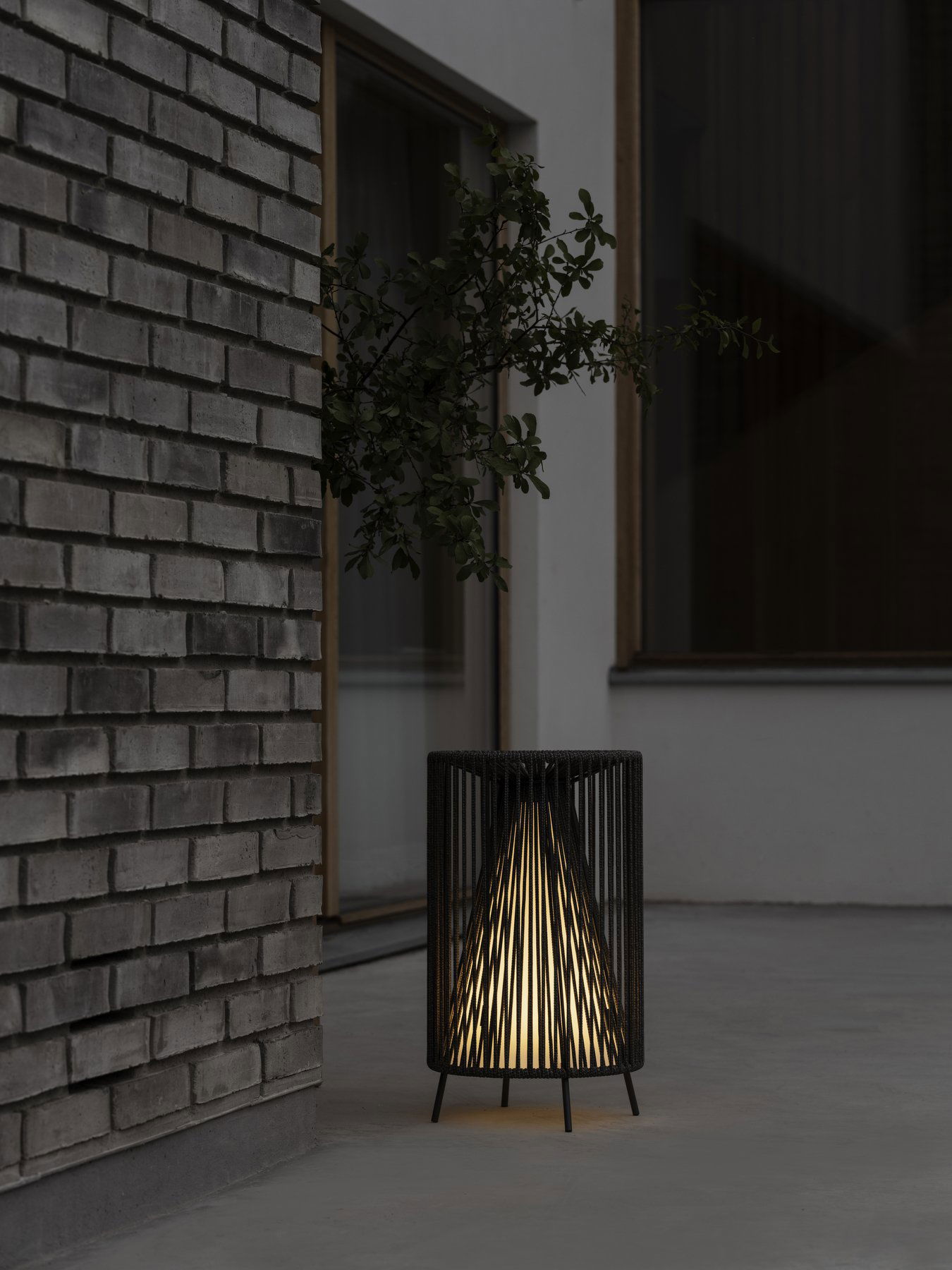 Moderne schwarze Lampe, die warmes Licht neben einer strukturierten Backsteinwand in einem minimalistischen Umfeld ausstrahlt.