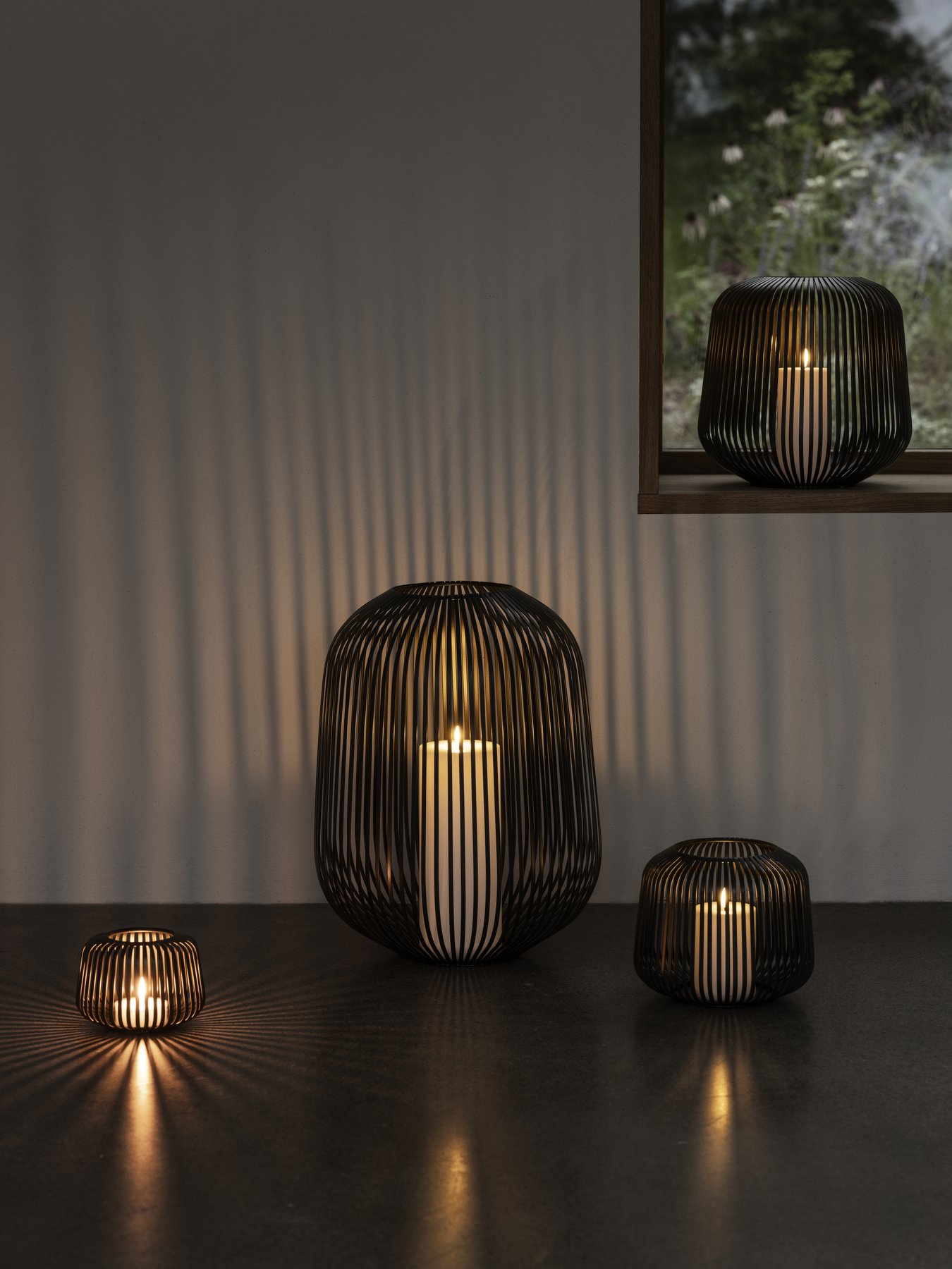 Elegante schwarze Drahtgeflechtlaternen, die sanfte, warme Kerzenlichtschatten in einer gemütlichen Umgebung werfen.