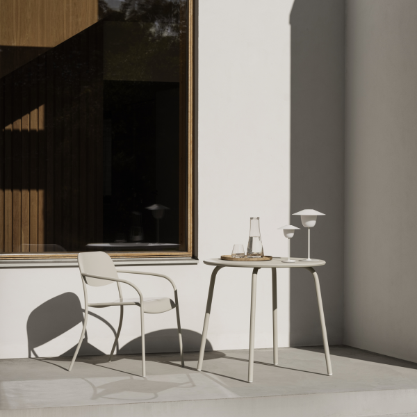 Moderne Außenszene mit einem minimalistischen Stuhl und Tisch sowie Glaswaren auf einer sonnendurchfluteten Terrasse.