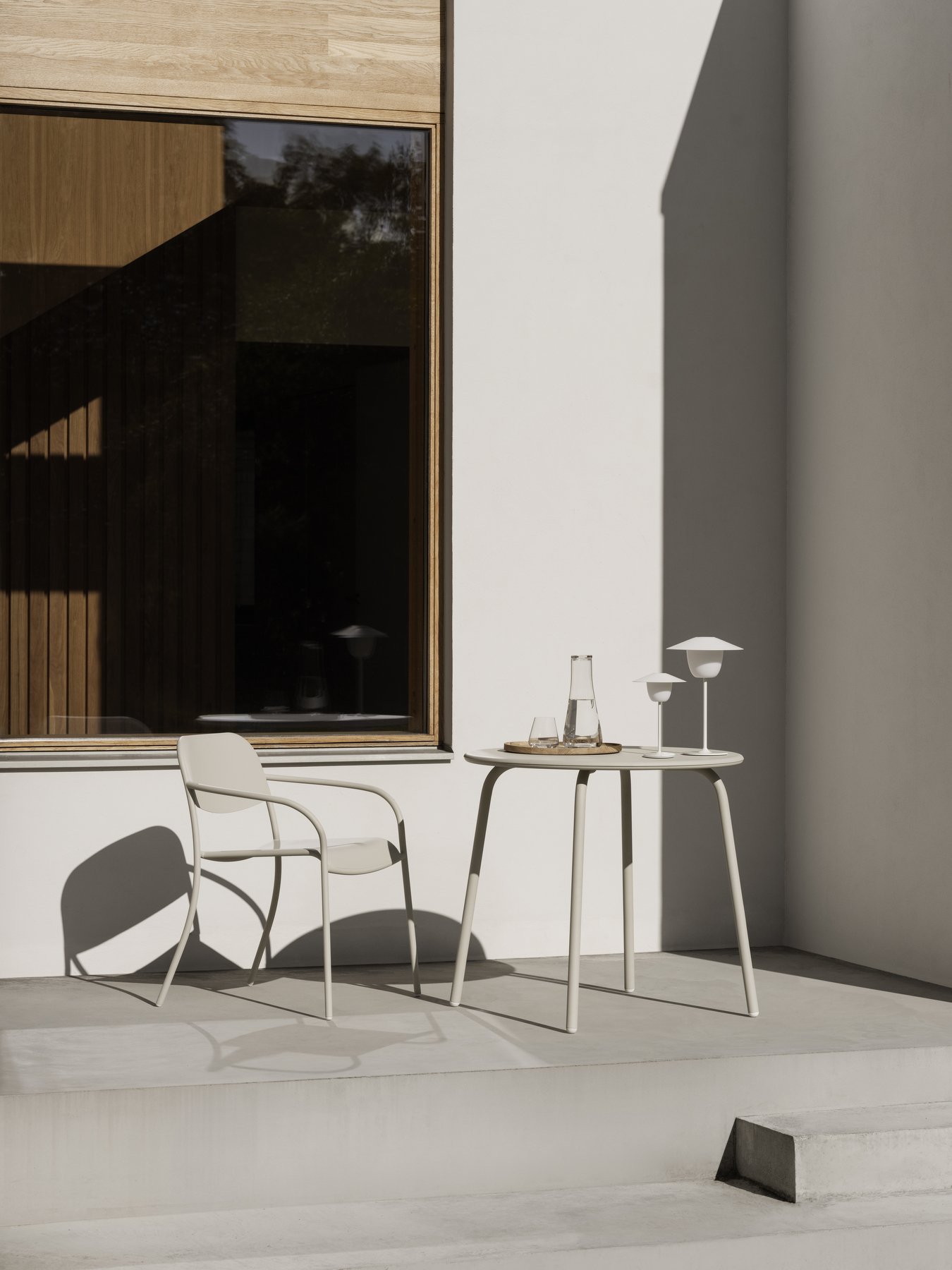 Moderne Außenszene mit einem minimalistischen Stuhl und Tisch sowie Glaswaren auf einer sonnendurchfluteten Terrasse.