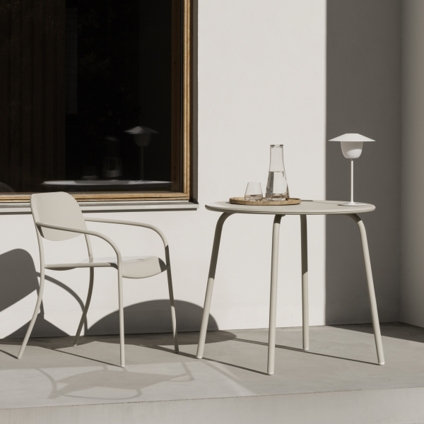 Modern outdoor dining setup with a white table, chair, and minimalist lamp.