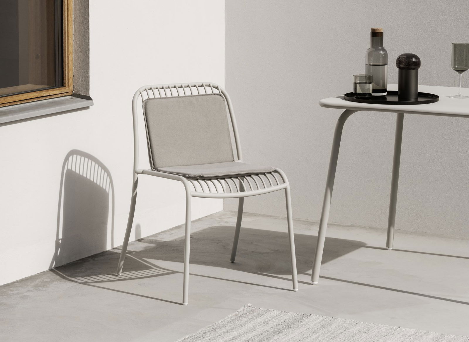 Stylischer weißer Stuhl mit grauem Kissen neben einem minimalistischen Tisch in einem modernen Umfeld.