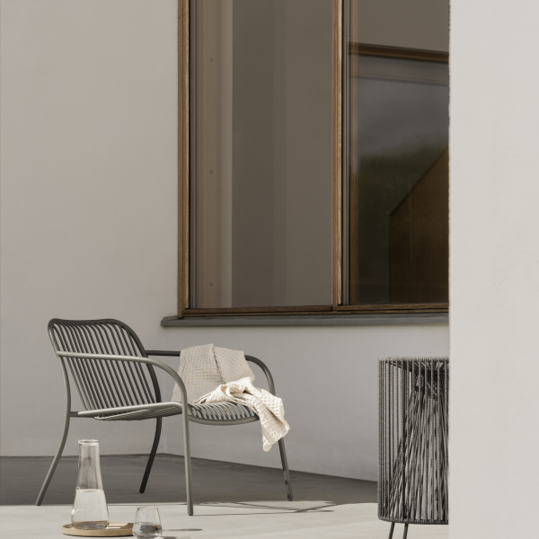Modern outdoor chair with a cozy blanket, accompanied by a glass and pitcher on a table.