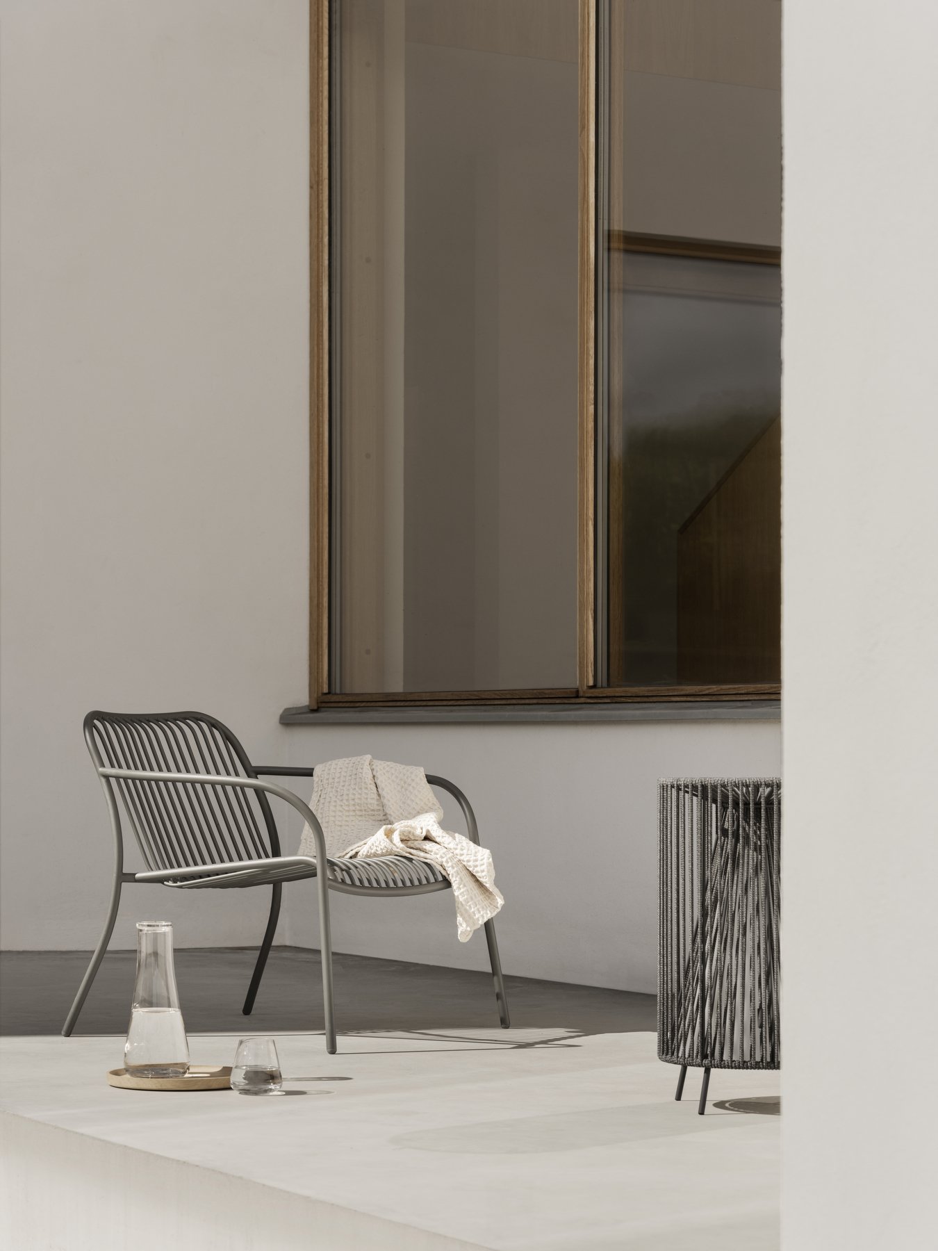 Modern outdoor chair with a cozy blanket, accompanied by a glass and pitcher on a table.