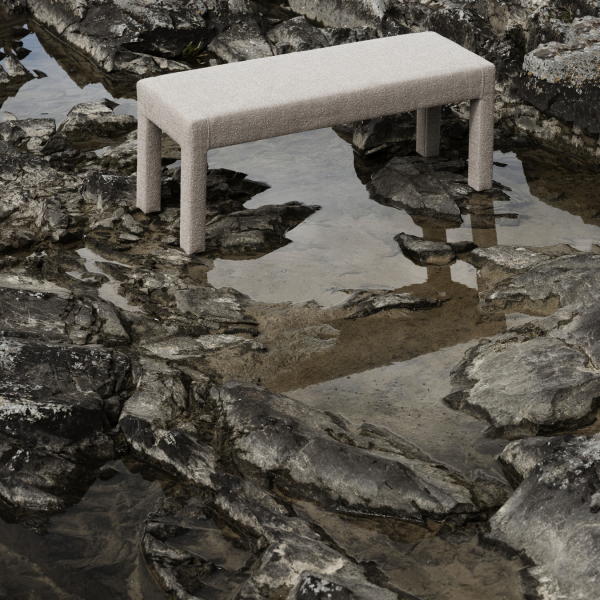 Eine stilvolle beige Bank auf felsigem Gelände, die sich im ruhigen Wasser spiegelt.