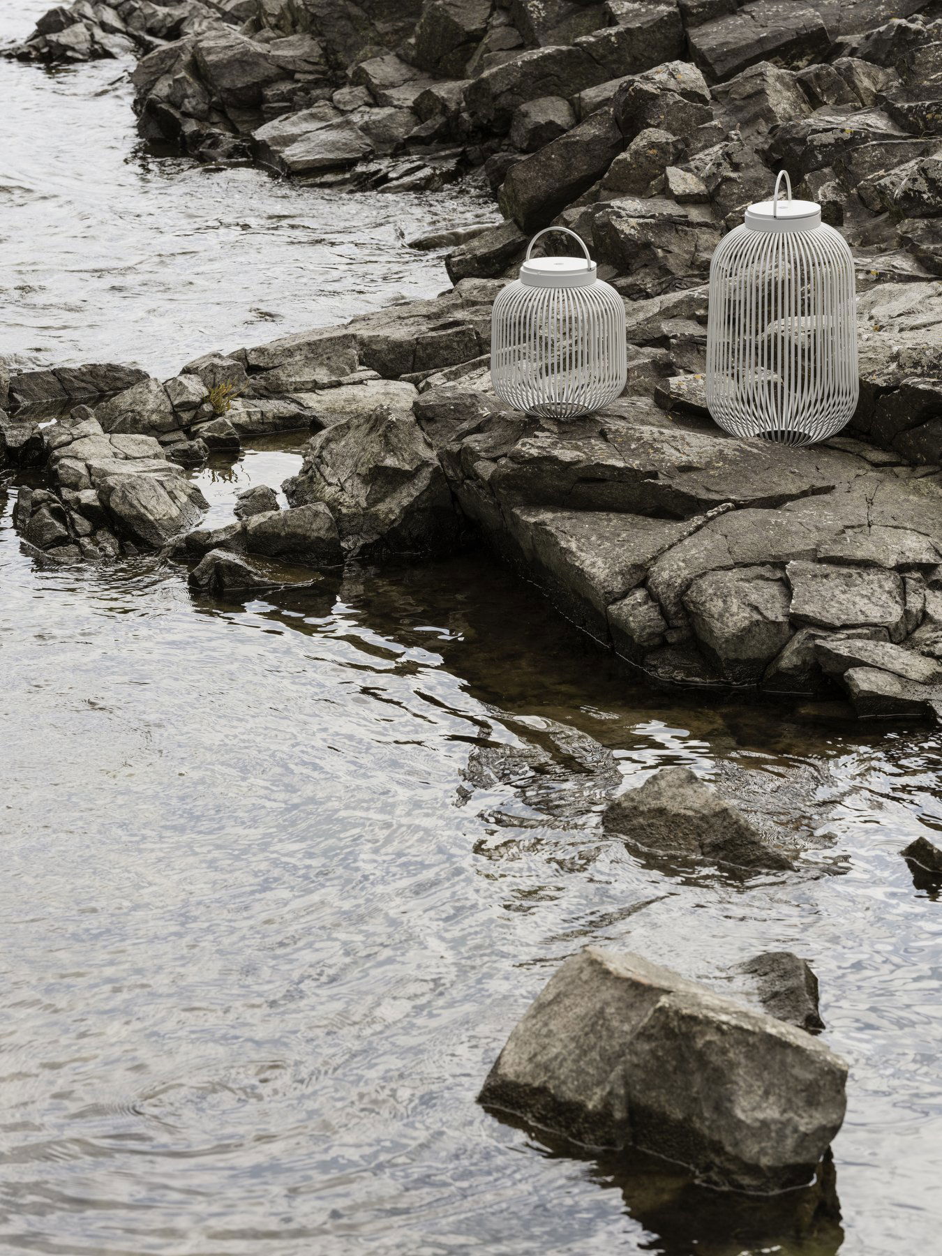 Elegant white lanterns on rocky shore beside tranquil water, enhancing natural scenery.
