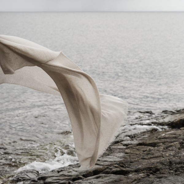 Flowing fabric gently swaying over rocky shoreline by a serene ocean.
