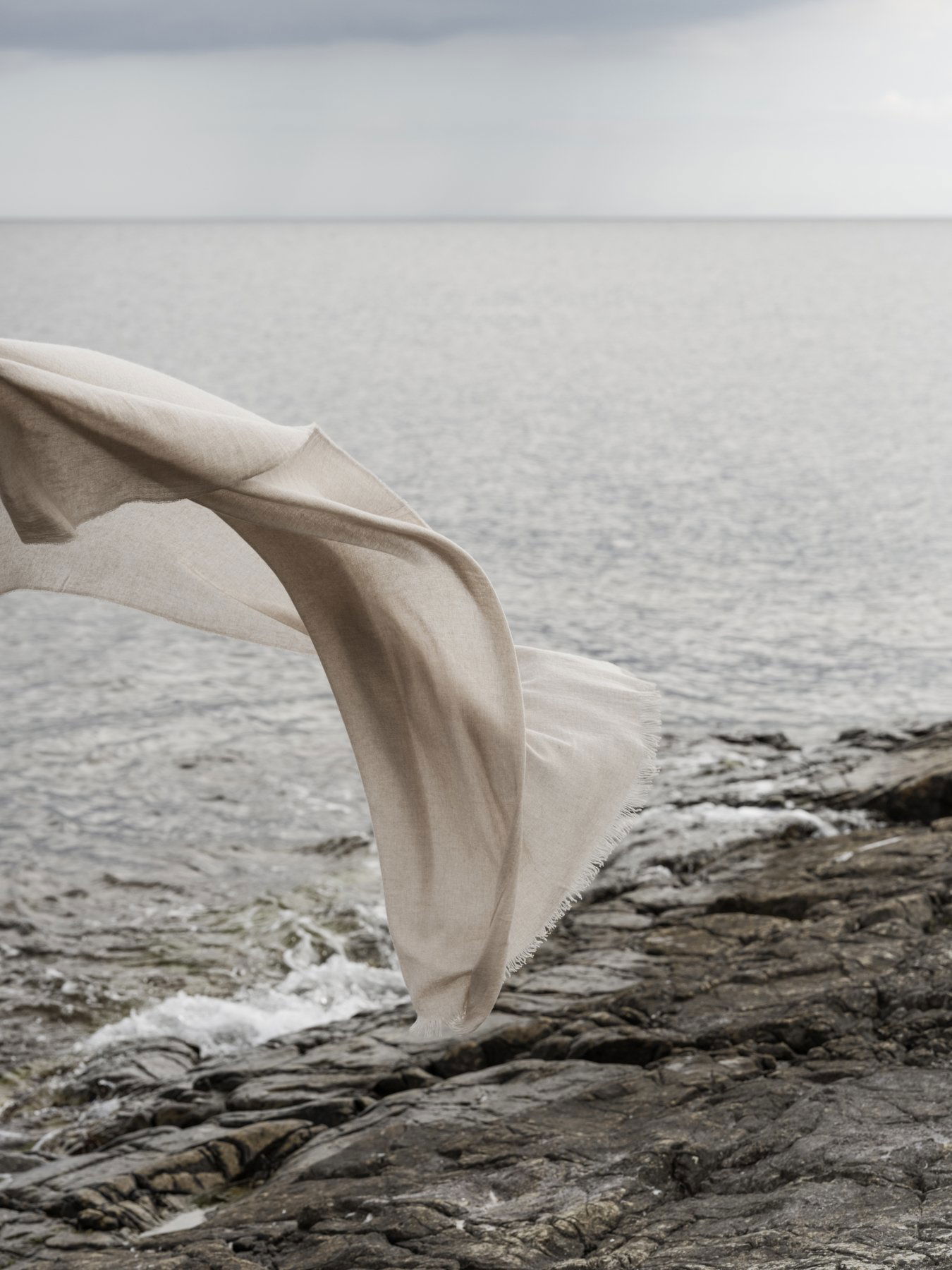 Flowing fabric gently swaying over rocky shoreline by a serene ocean.