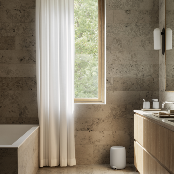 Modern bathroom featuring natural stone walls, a soaking tub, and large window with white curtains.