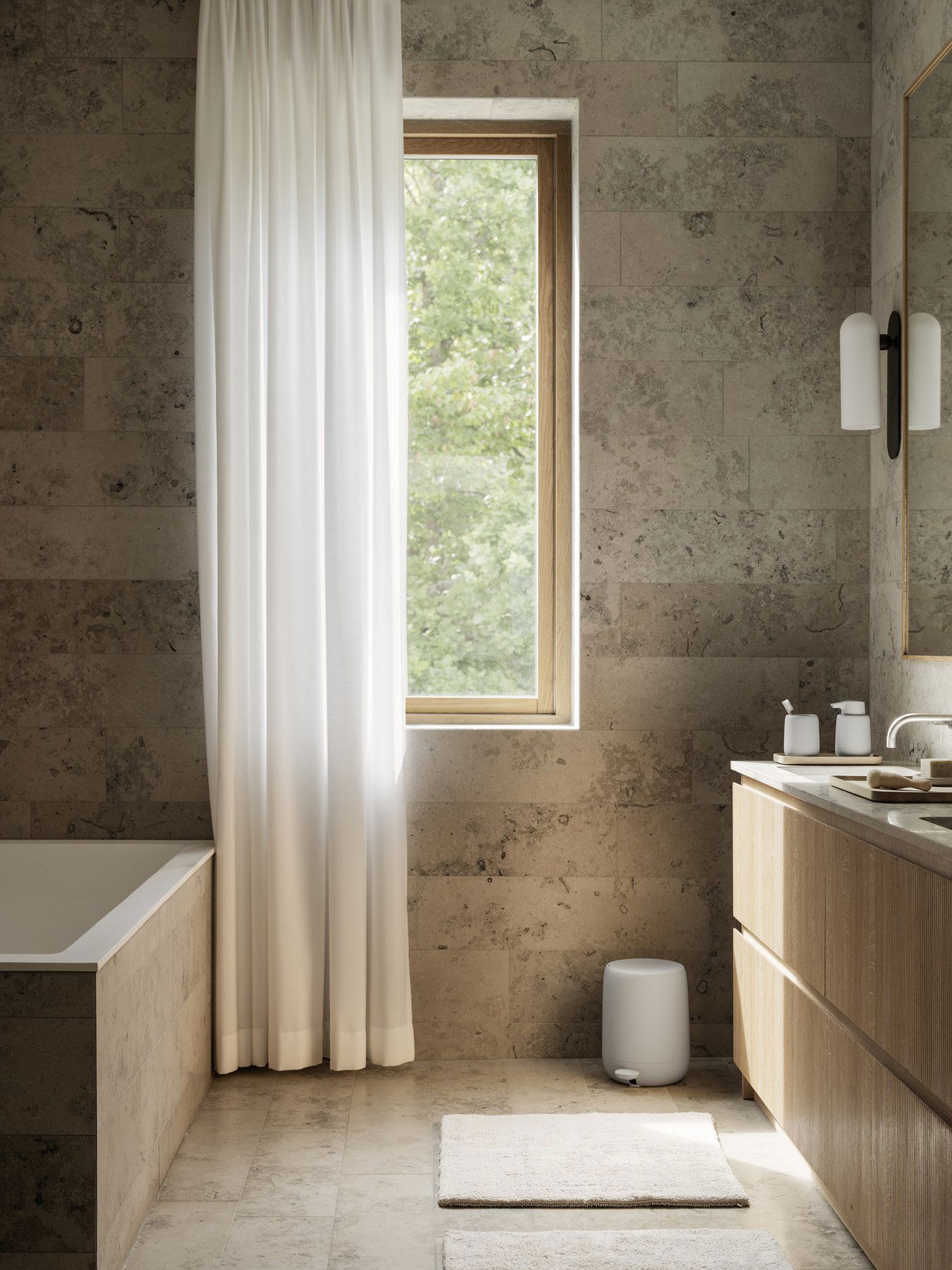 Modern bathroom featuring natural stone walls, a soaking tub, and large window with white curtains.