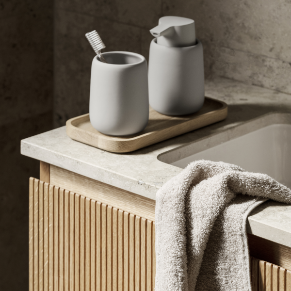 Moderne Badezimmerausstattung mit grauen Accessoires, einem Holztablett und einem weichen Handtuch auf der Arbeitsplatte.
