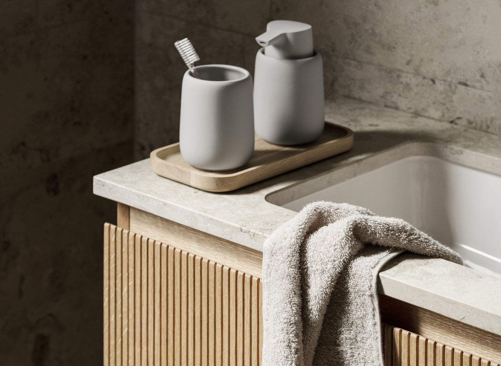 Moderne Badezimmerausstattung mit grauen Accessoires, einem Holztablett und einem weichen Handtuch auf der Arbeitsplatte.