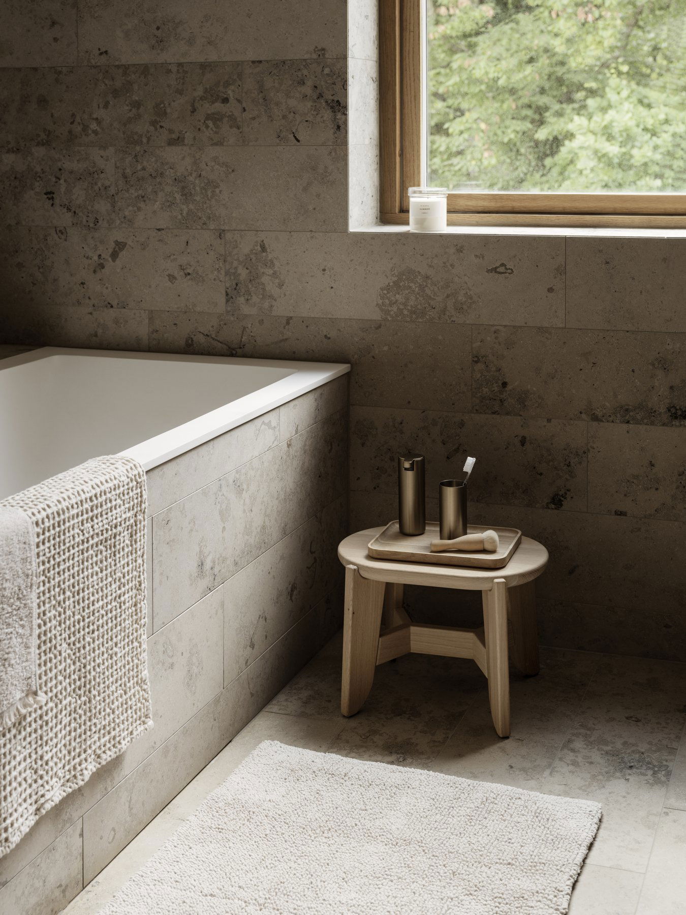 Minimalist bathroom with a soaking tub, natural wood stool, and soft linen towel.