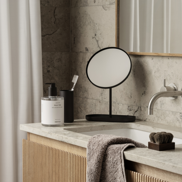 Modernes Badezimmer mit einem runden Spiegel, eleganten Armaturen und ordentlich angeordneten Toilettenartikeln.