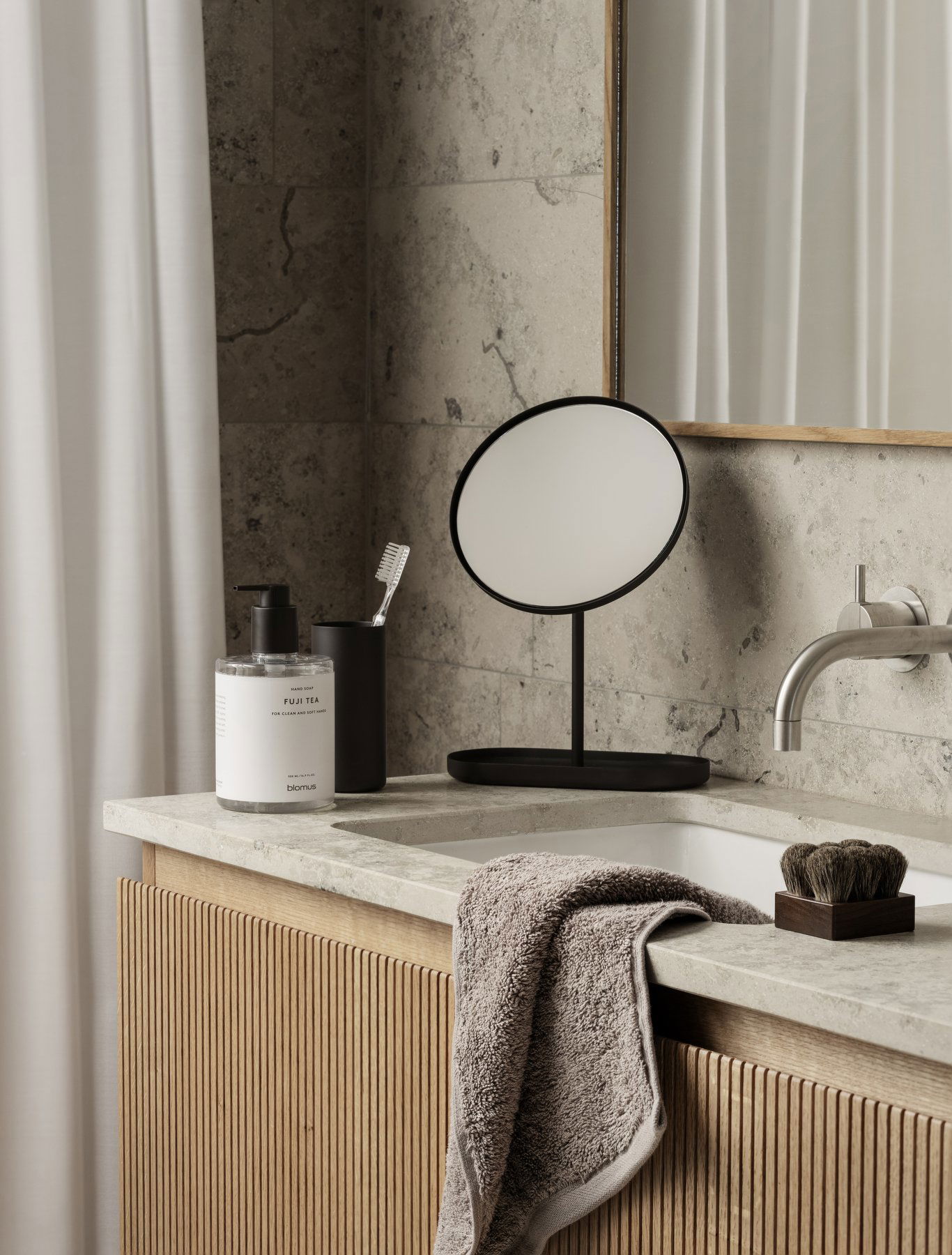 Modernes Badezimmer mit einem runden Spiegel, eleganten Armaturen und ordentlich angeordneten Toilettenartikeln.