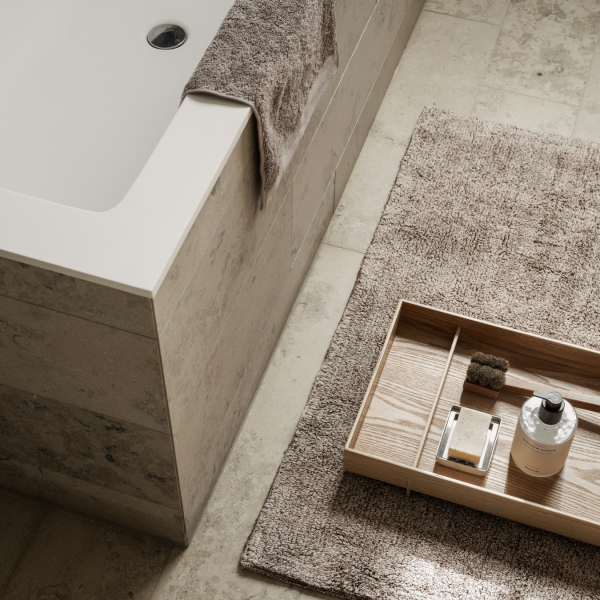 Modern bathroom decor featuring a bathtub, wooden tray, and textured rug for relaxation.