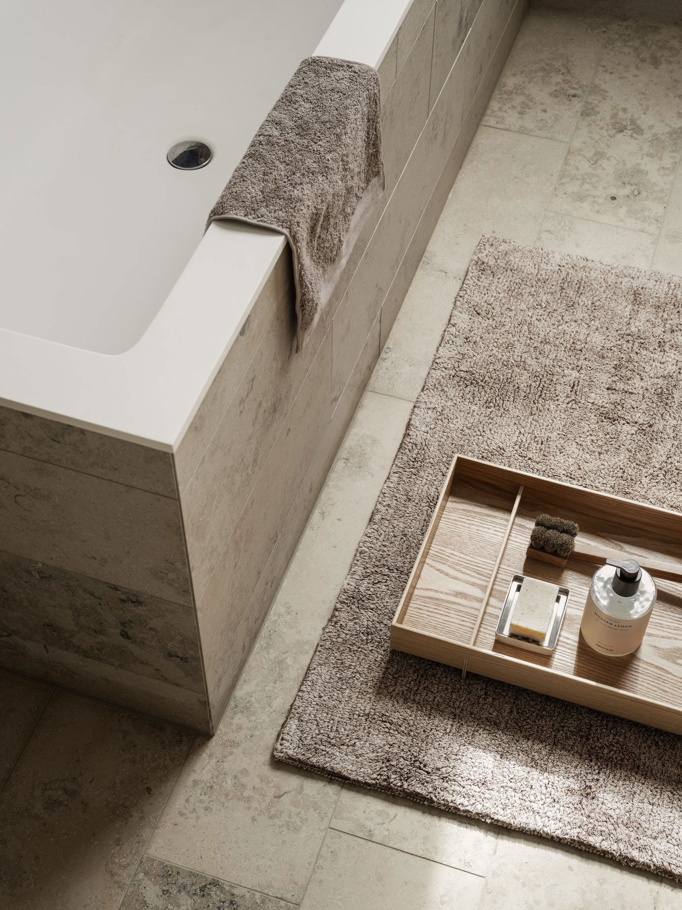 Modern bathroom decor featuring a bathtub, wooden tray, and textured rug for relaxation.