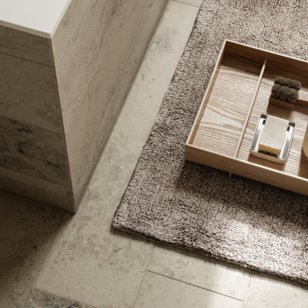 Elegant bathroom decor featuring a wooden tray on a cozy rug and natural stone tiles.