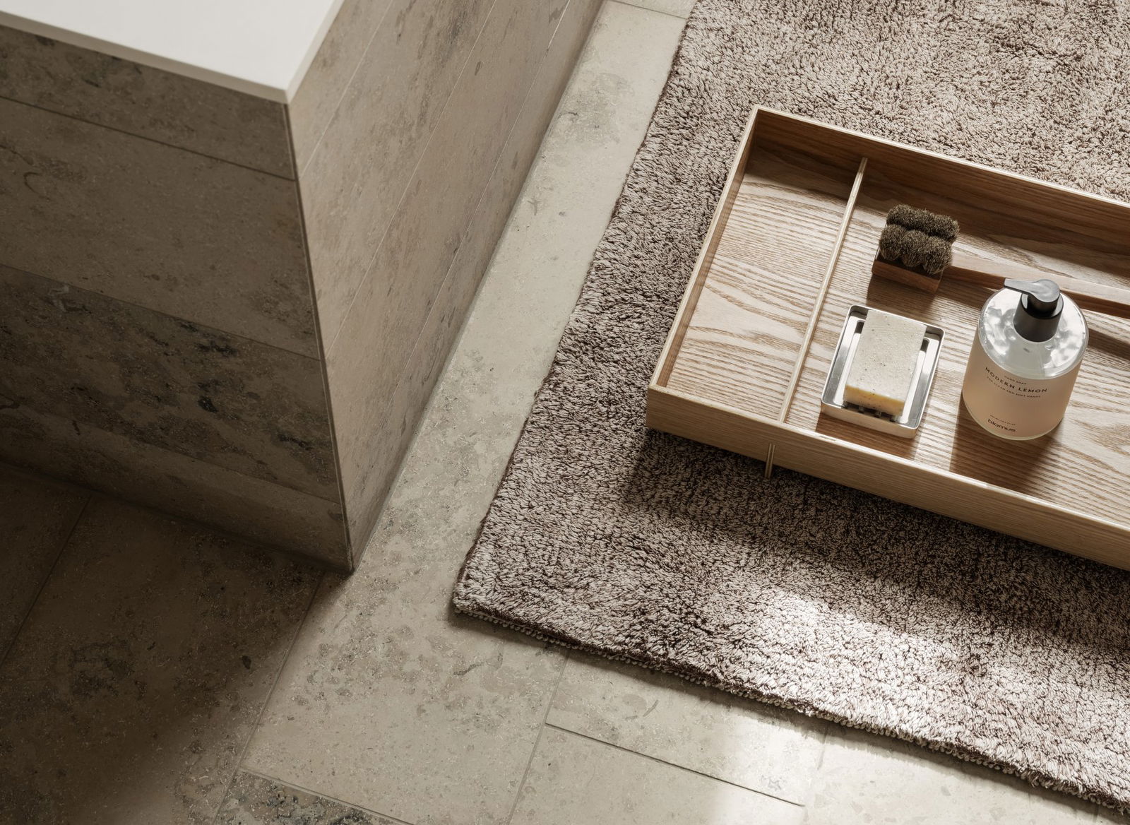 Elegant bathroom decor featuring a wooden tray on a cozy rug and natural stone tiles.