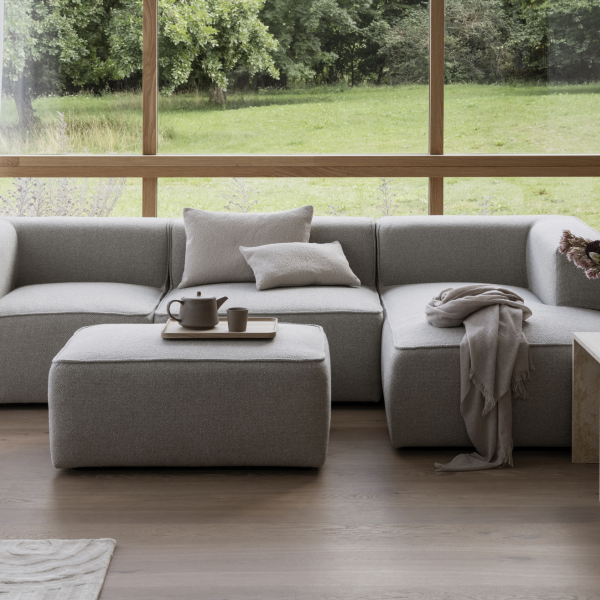 Gemütliches modernes Wohnzimmer mit einem grauen Ecksofa und natürlichem Licht von großen Fenstern.