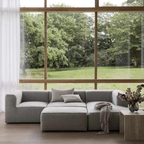 Moderner grauer Sofa in einem hellen Wohnzimmer mit großen Fenstern, die auf eine grüne Landschaft blicken.