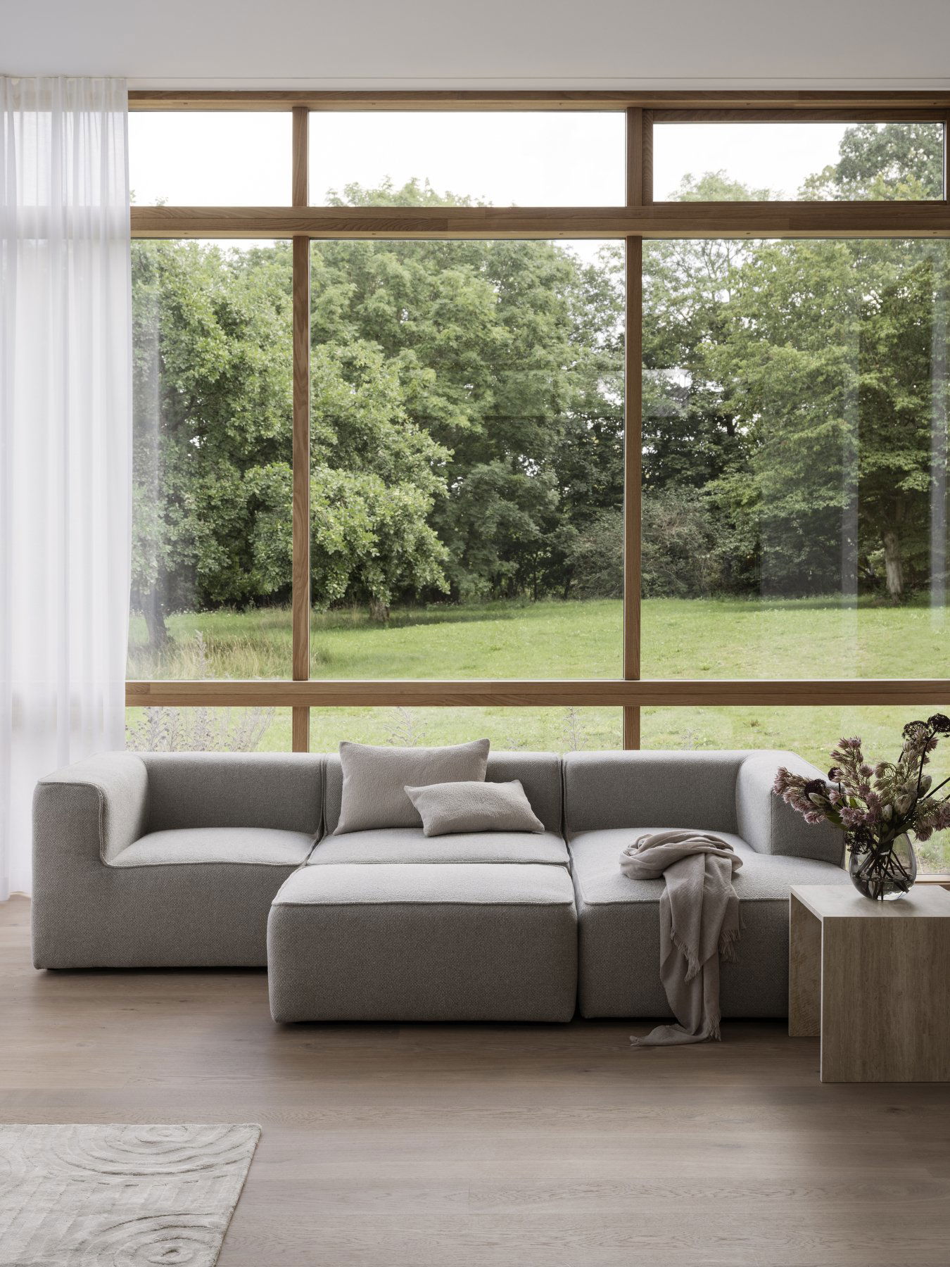 Moderner grauer Sofa in einem hellen Wohnzimmer mit großen Fenstern, die auf eine grüne Landschaft blicken.