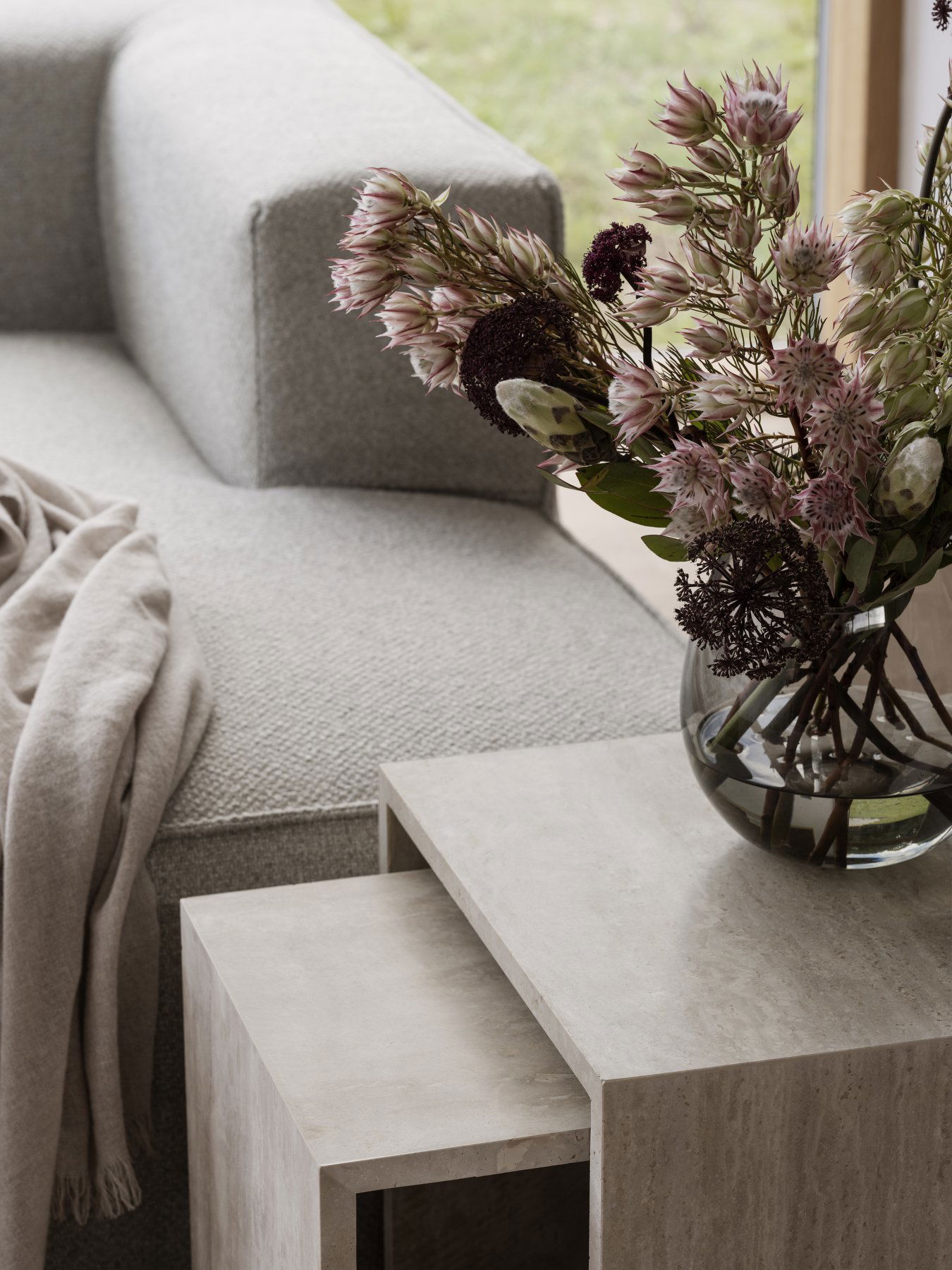Cozy living room scene with a gray sofa, soft throw, and floral arrangement on a side table.