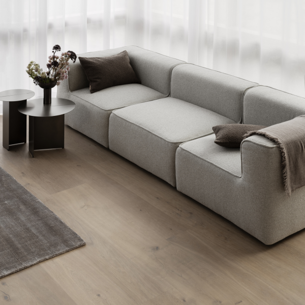 Modern gray sofa with cushions and side tables in a bright, minimalistic living room.